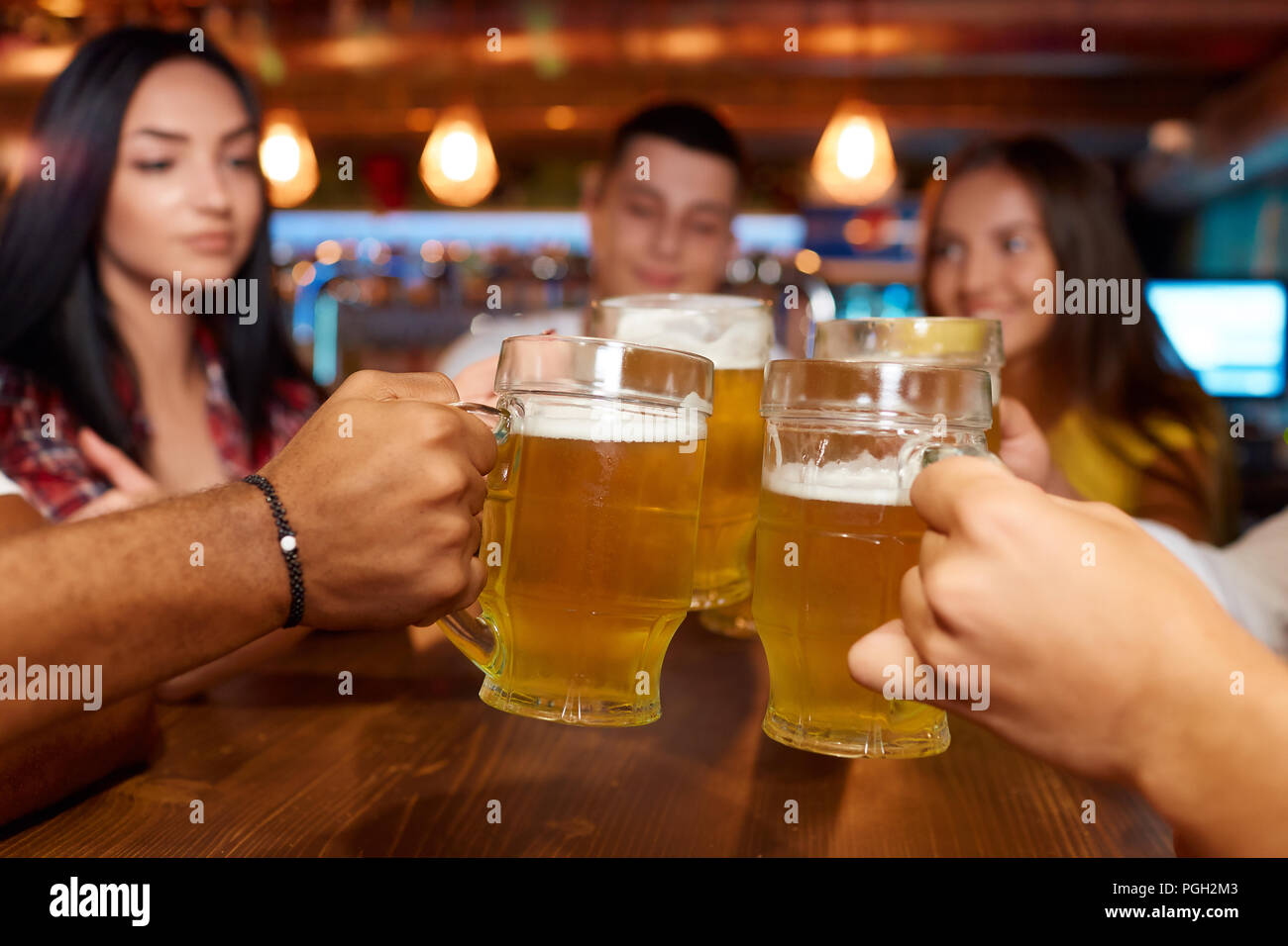 Vier Freunde Toasten mit Gläser helles Bier im Pub. Gruppe Leute Bier trinken, sich gemeinsam amüsiert, die Bier anstoßen Tabelle oben Stockfoto
