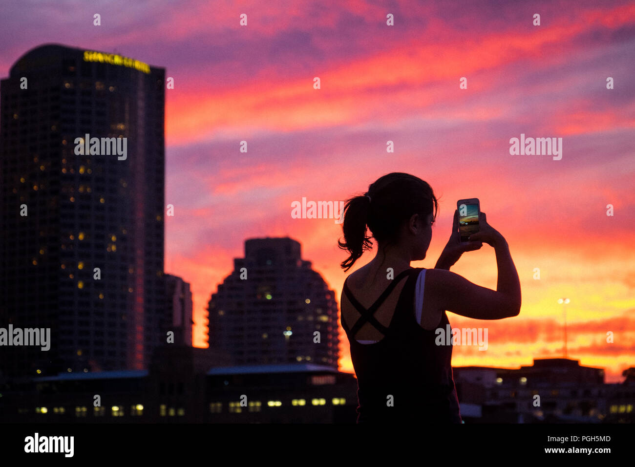 Eine Frau, die ein Panorama Foto auf Ihrem Smartphone auf den Sonnenuntergang über Sydney Harbour Bridge, Australien Stockfoto