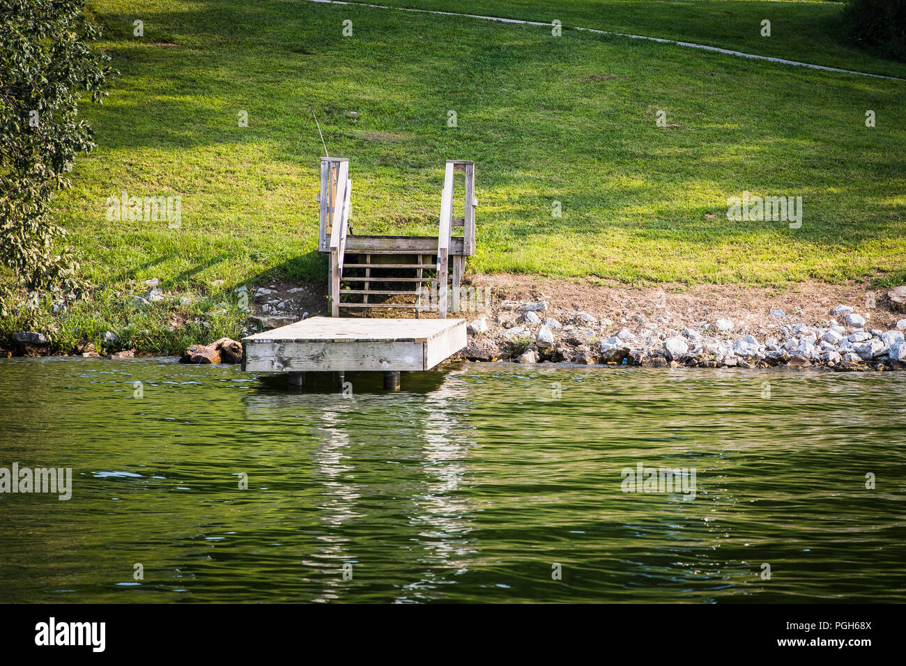 Holz Dock an einem See im Sommer von grünem Gras und Bäumen umgeben. Stockfoto