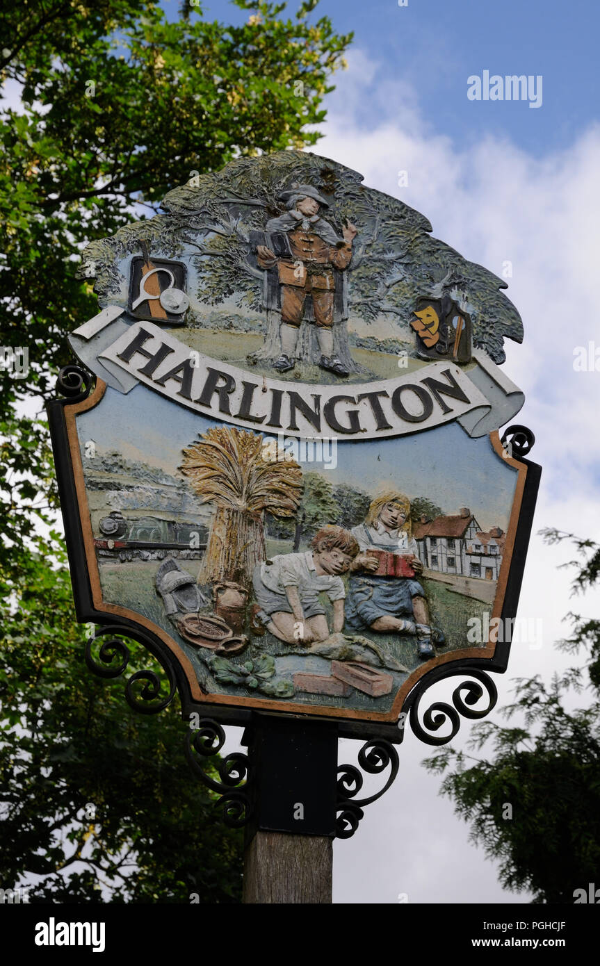 Ortsschild Harlington, Bedfordshire. Elemente in der Gestaltung porträtieren Harlington der Geschichte, darunter John Bunyan Verkündigung unter der Eiche. Stockfoto