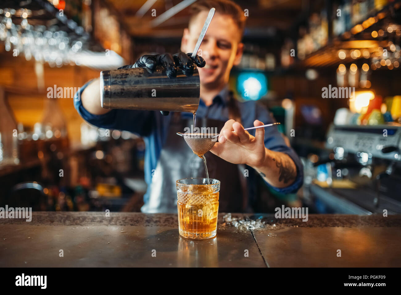 Männliche Barkeeper Schürze gießt aus einem Getränk durch ein Sieb in ein Glas. Der Barkeeper an der Theke. Alkohol Getränke Vorbereitung Stockfoto