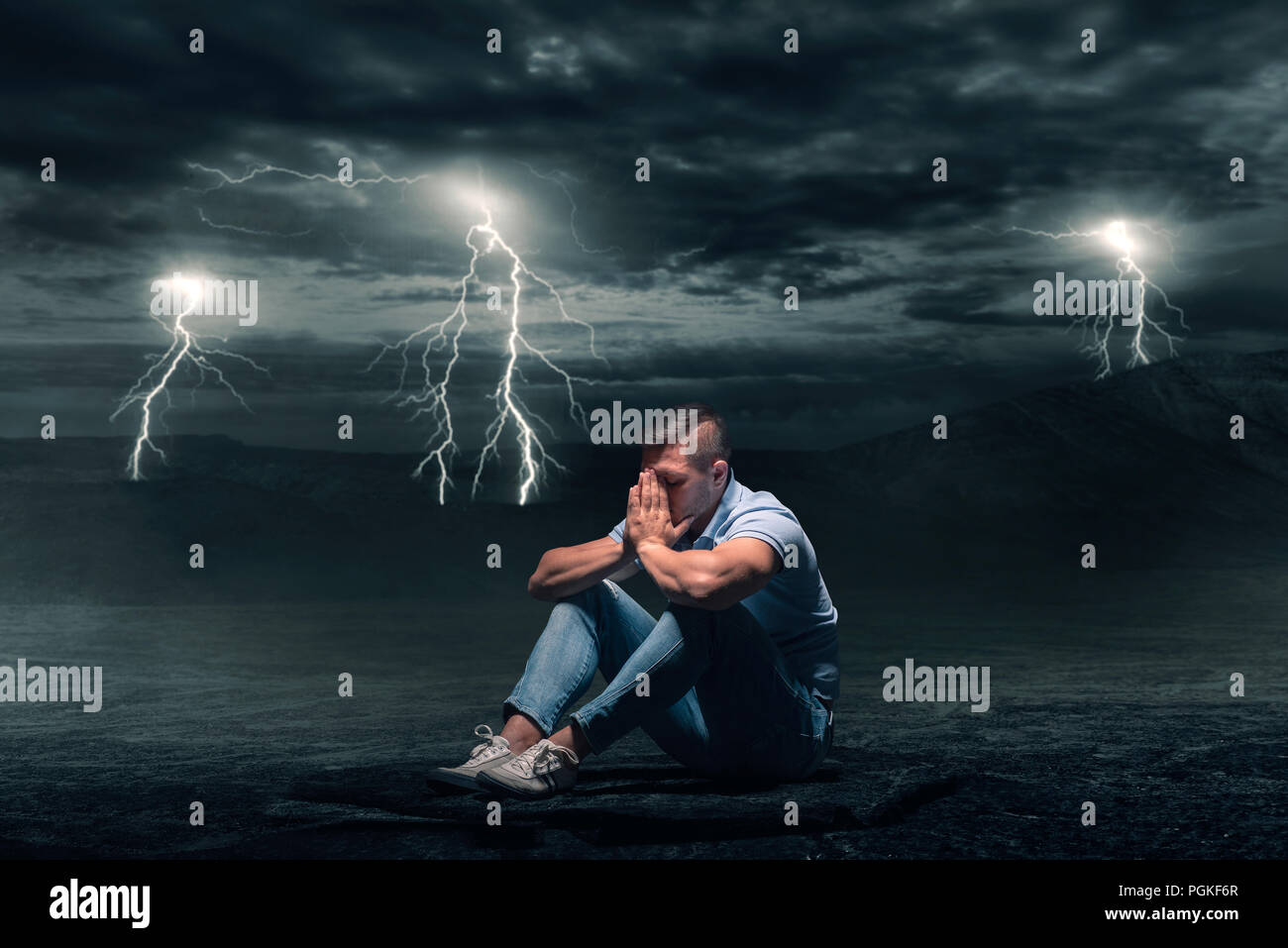 Junger Mann auf dem Boden sitzend in der Wüste, Sturm mit Blitz auf Hintergrund Stockfoto