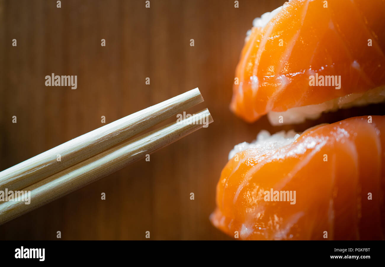 Verfügbare Bambus Stäbchen und Lachs sushi Close-up auf hölzernen Hintergrund Stockfoto