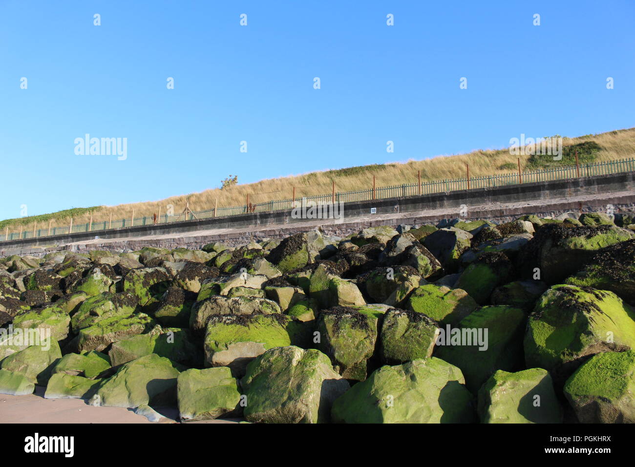 Rock Rüstung auf einem Strand vor einer Eisenbahnstrecke mit einem klaren Himmel verwendet Stockfoto