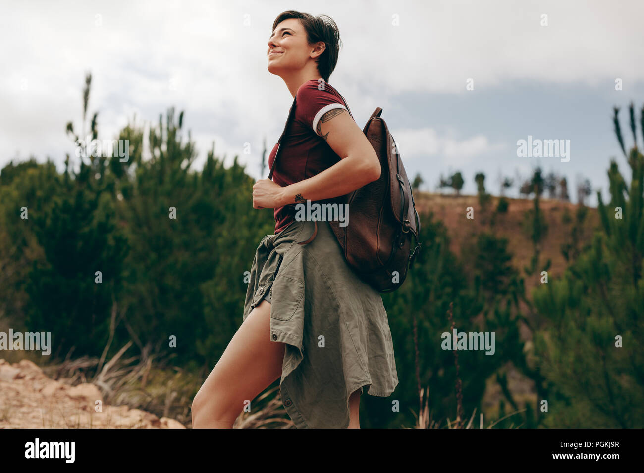 Gerne Frau wandern in einem Wald. Frau, die eine Tasche zu Fuß durch den Wald mit Bäumen im Hintergrund Stockfoto