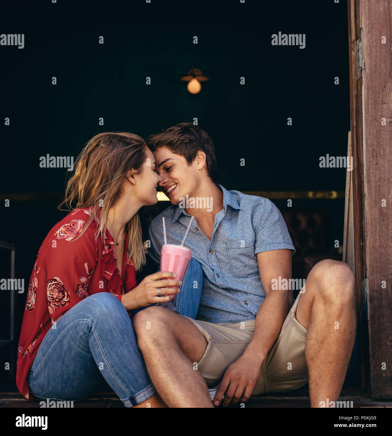 Mann und Frau zusammen sitzen berühren ihre Köpfe halten ein Glas Milchshake. Verliebtes Paar in einem Restaurant draußen sitzen. Stockfoto