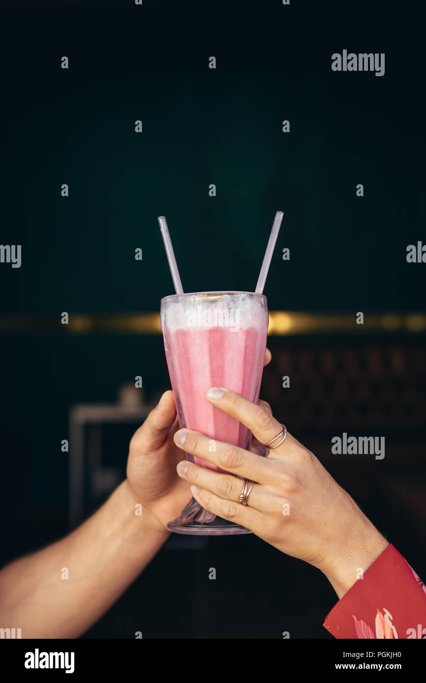 In der Nähe der Hände von ein Paar hält ein Glas Milchshake mit zwei strohhalme. Stockfoto
