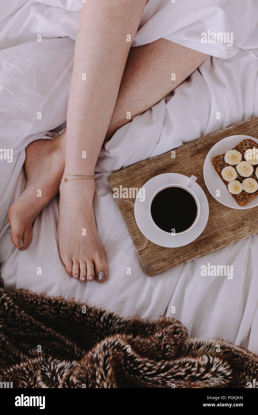 Nahaufnahme Beine einer Frau schlafen im Bett mit Frühstück durch ihre Seite. Frühstück mit Kaffee schwarz platziert neben eine Frau schlafend auf dem Bett. Stockfoto