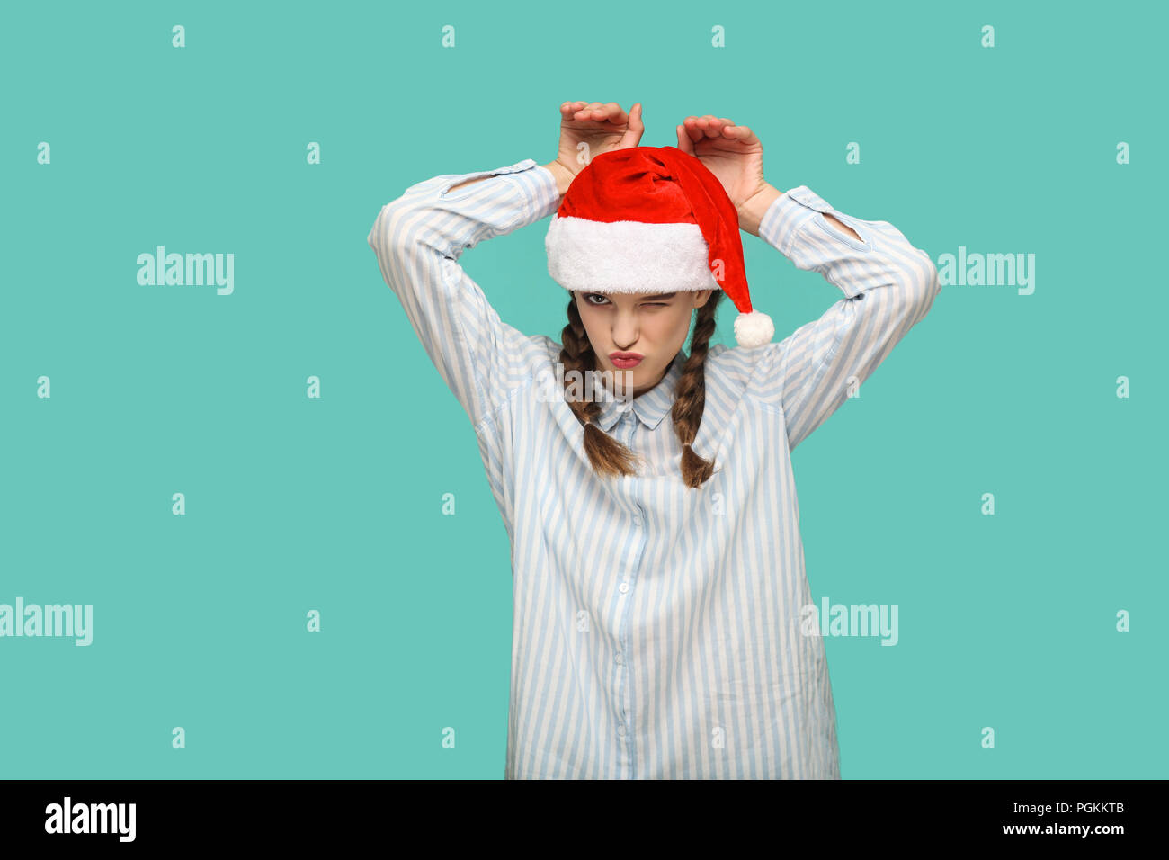 Neues Jahr Konzept. lustige schönes Mädchen in Hellblau T-Shirt in Red christmas Cap mit Bunny Geste gestreift, winking, Küssen und auf c Stockfoto