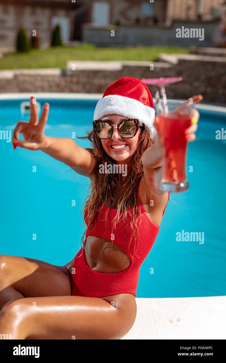 Junge schöne Frau in der Nähe des Pool in Santa Claus hat feiern Silvester und Weihnachten in heißes Land mit einem Glas Cocktail. Stockfoto