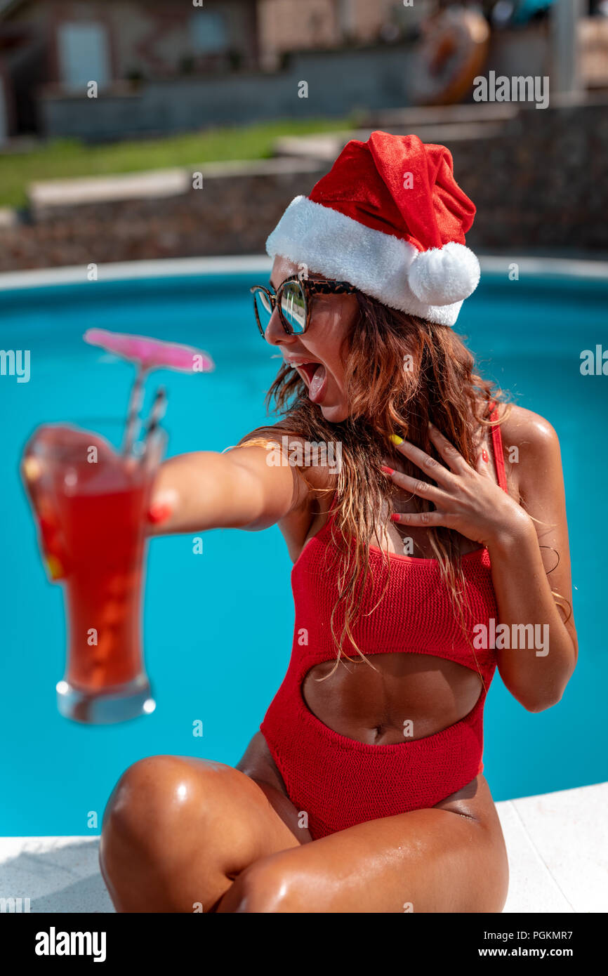 Junge schöne Frau in der Nähe des Pool in Santa Claus hat feiern Silvester und Weihnachten in heißes Land mit einem Glas Cocktail. Stockfoto