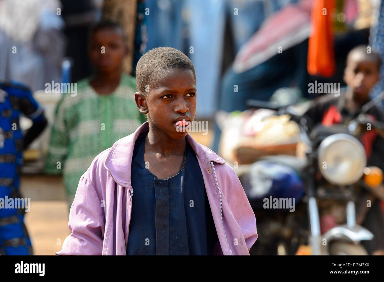 BOHICON, BENIN - Jan 12, 2017: Unbekannter beninischen Jungen in lila Jacke zeigt eine Zunge auf dem lokalen Markt. Benin Kinder leiden der Armut aufgrund Stockfoto