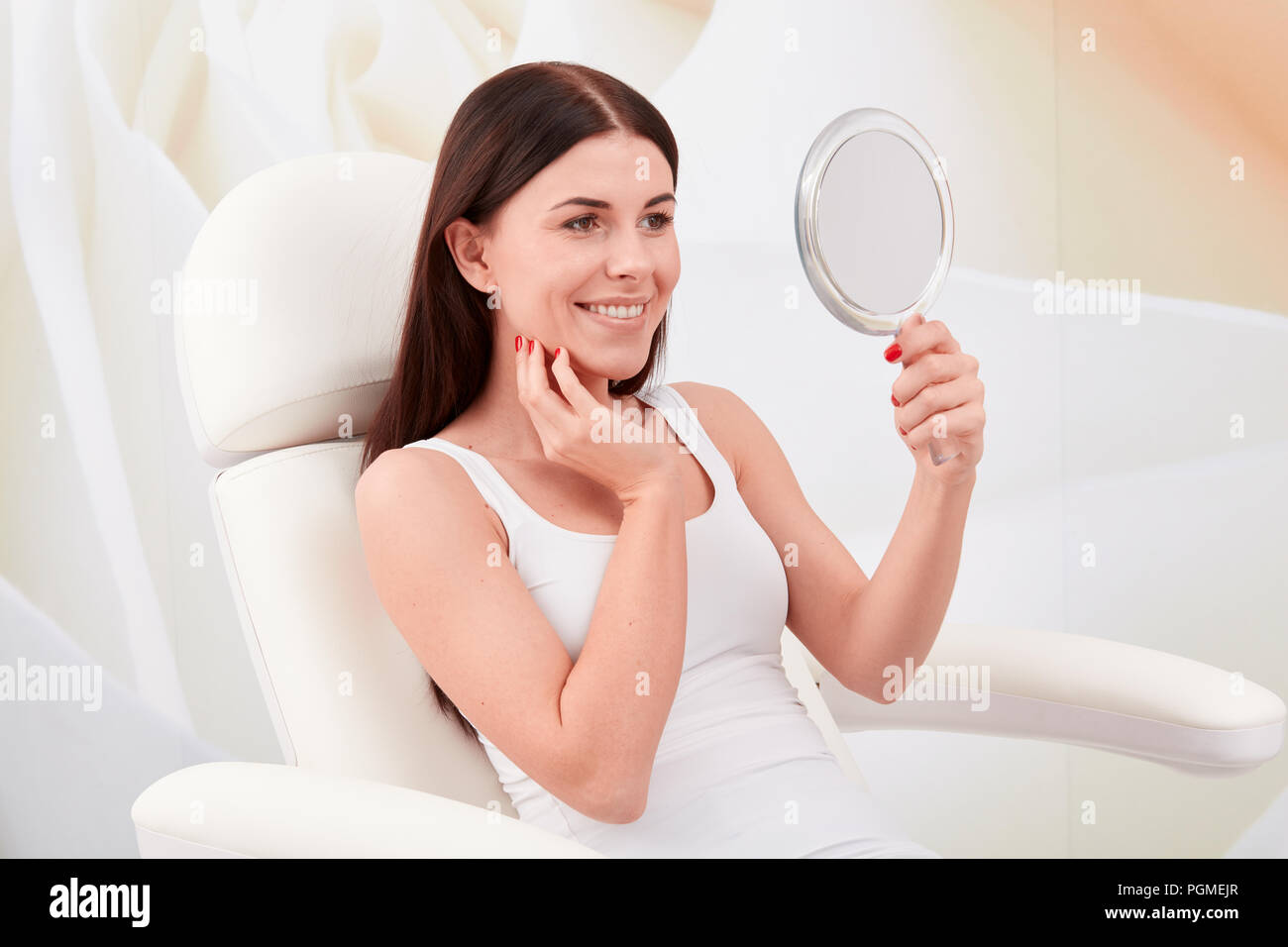 Kosmetische Behandlungen in einem professionellen kosmetischen Klinik - eine junge Frau sieht ihr Gesicht im Spiegel Stockfoto