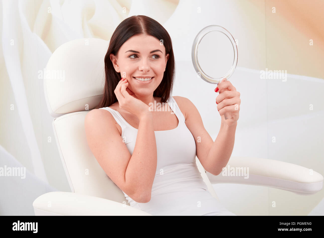 Kosmetische Behandlungen in einem professionellen kosmetischen Klinik - eine junge Frau sieht ihr Gesicht im Spiegel Stockfoto