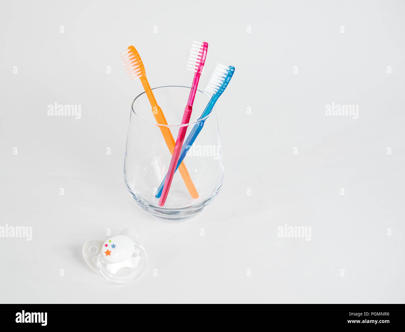 Drei Zahnbürsten in ein Glas mit Baby Schnuller auf weißem Hintergrund Stockfoto