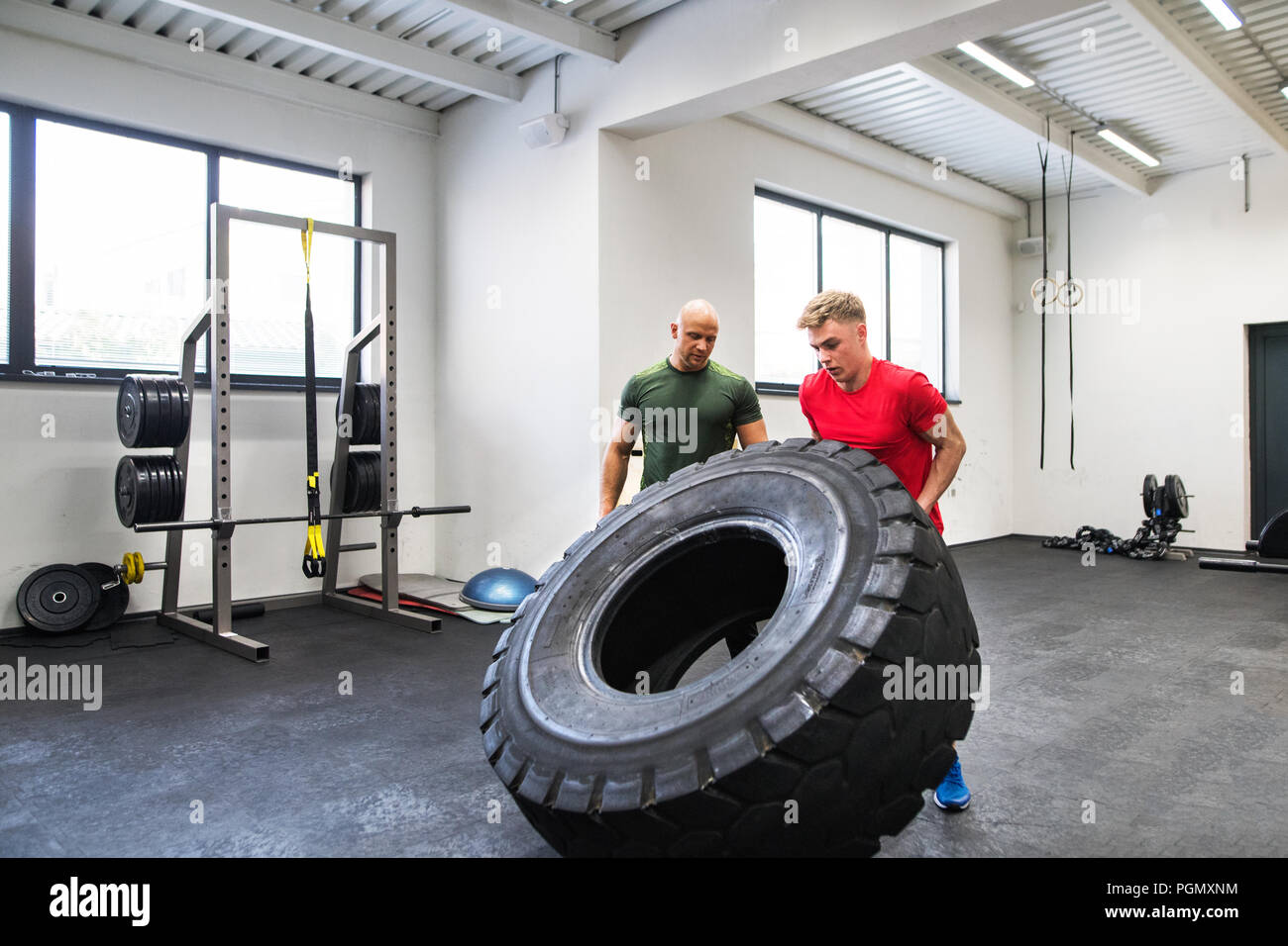 Passen junge Mann mit einem persönlichen Trainer im Fitnesscenter trainieren, Bewegen von großen Reifen. Stockfoto