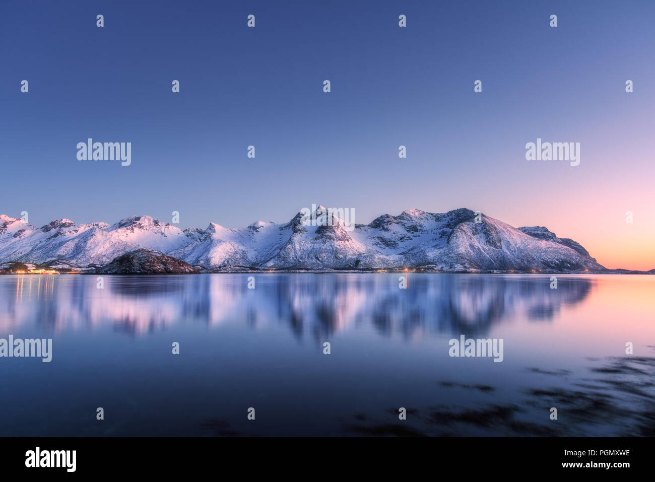 Schönen verschneiten Bergen und bunten Himmel im Wasser in der Nacht wider. Winterlandschaft mit Blick auf das Meer, die verschneite Felsen, blauer Himmel, Reflexion, Sonnenlicht Stockfoto