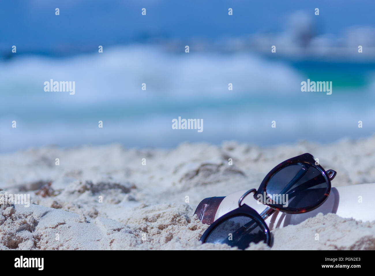Sommer Snapshot. Sonnencreme und Sonnenbrille im Sand. Fokus auf Gläsern details. Karibische Meer im Hintergrund. Stockfoto