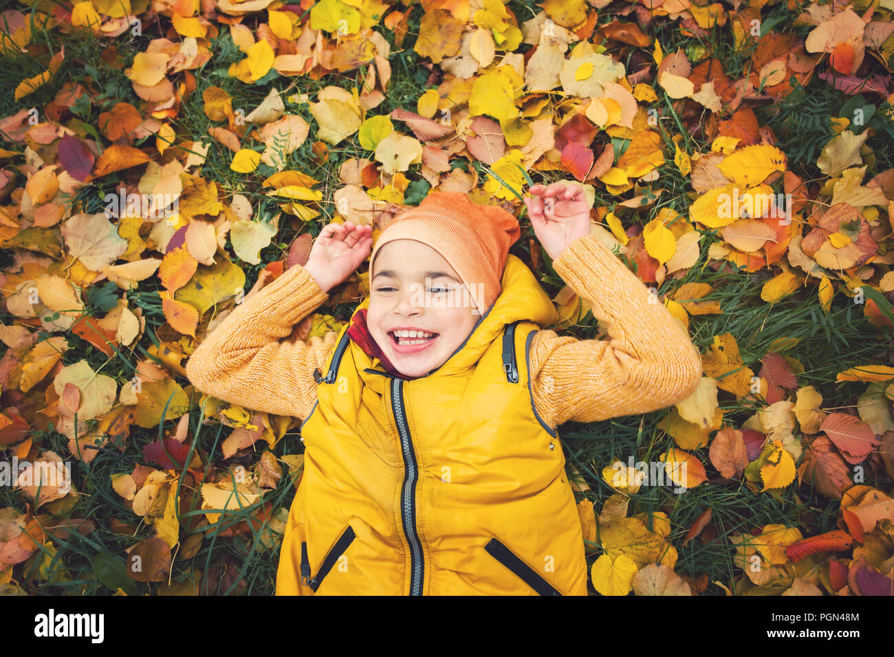 Kind lachen. Glückliches Kind Junge liegend auf Blätter im Herbst, Porträt Stockfoto