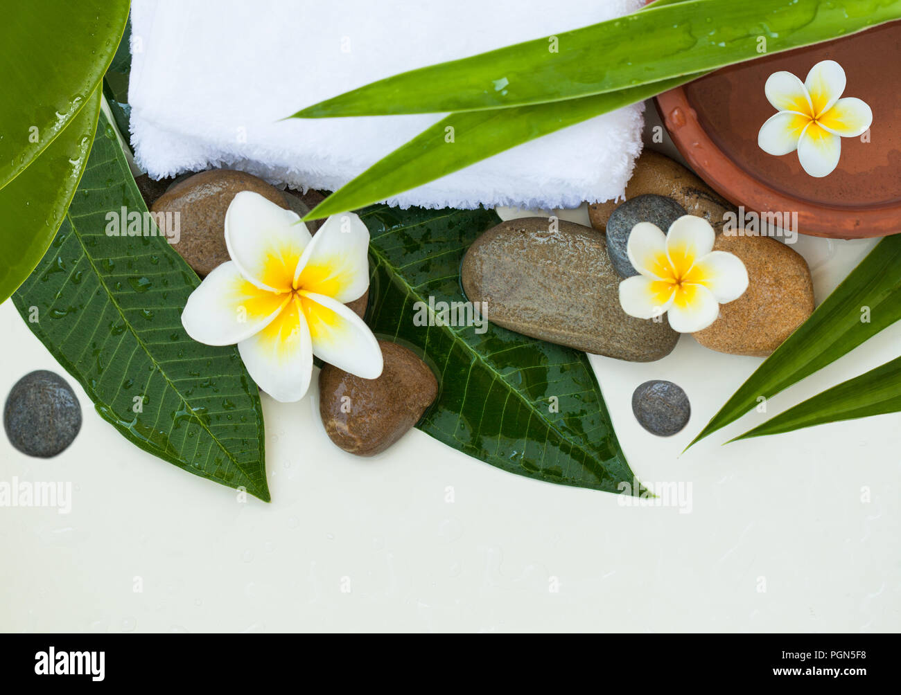 Spa, Wellness oder Hintergrund mit weißer Bettwäsche, tropische Blätter, Blumen und Steine. Stockfoto