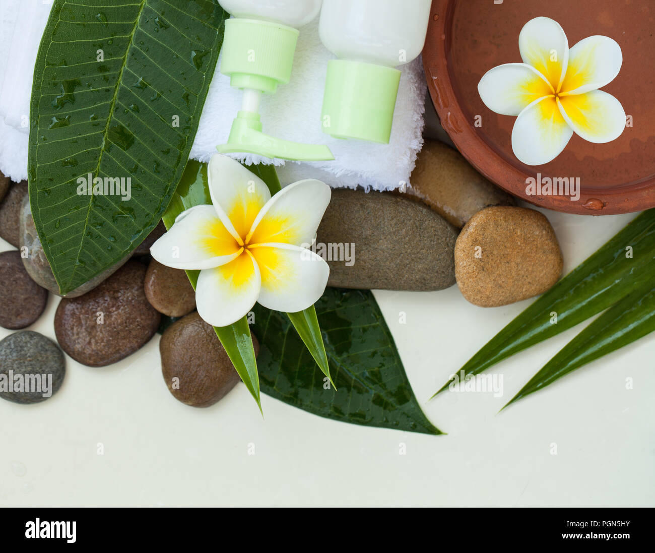 Wellness Hintergrund mit weißer Bettwäsche, tropische Blätter, Blumen, Körper- und Gesichtspflege Tools, Steine und Zubehör auf weißem Hintergrund, Ansicht von oben. Stockfoto