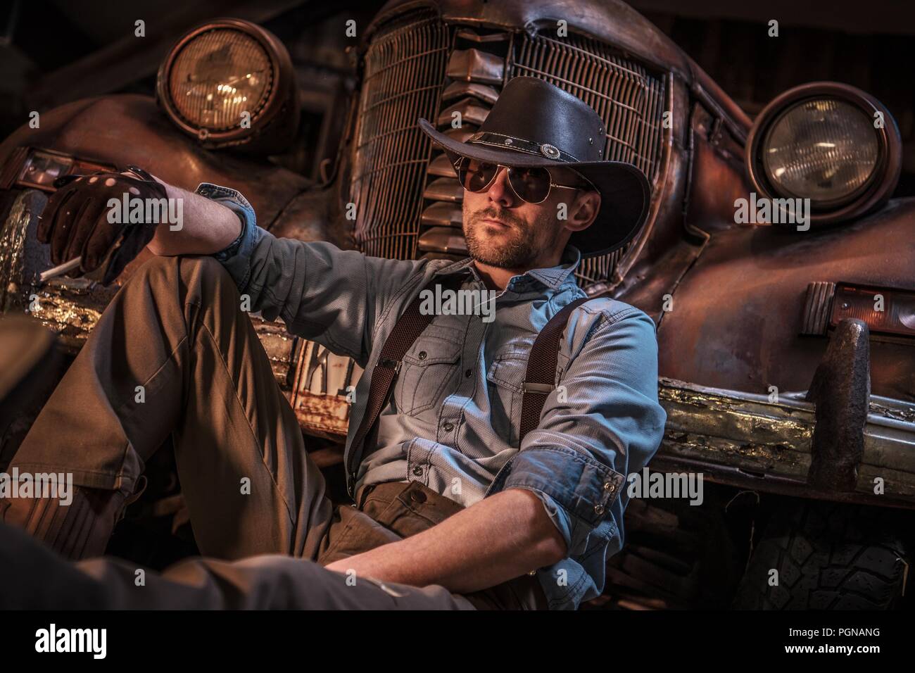 Kaukasische Cowboy Scheune entspannen. Amerikanische Männer vor der Alten rostigen Fahrzeug. Stockfoto