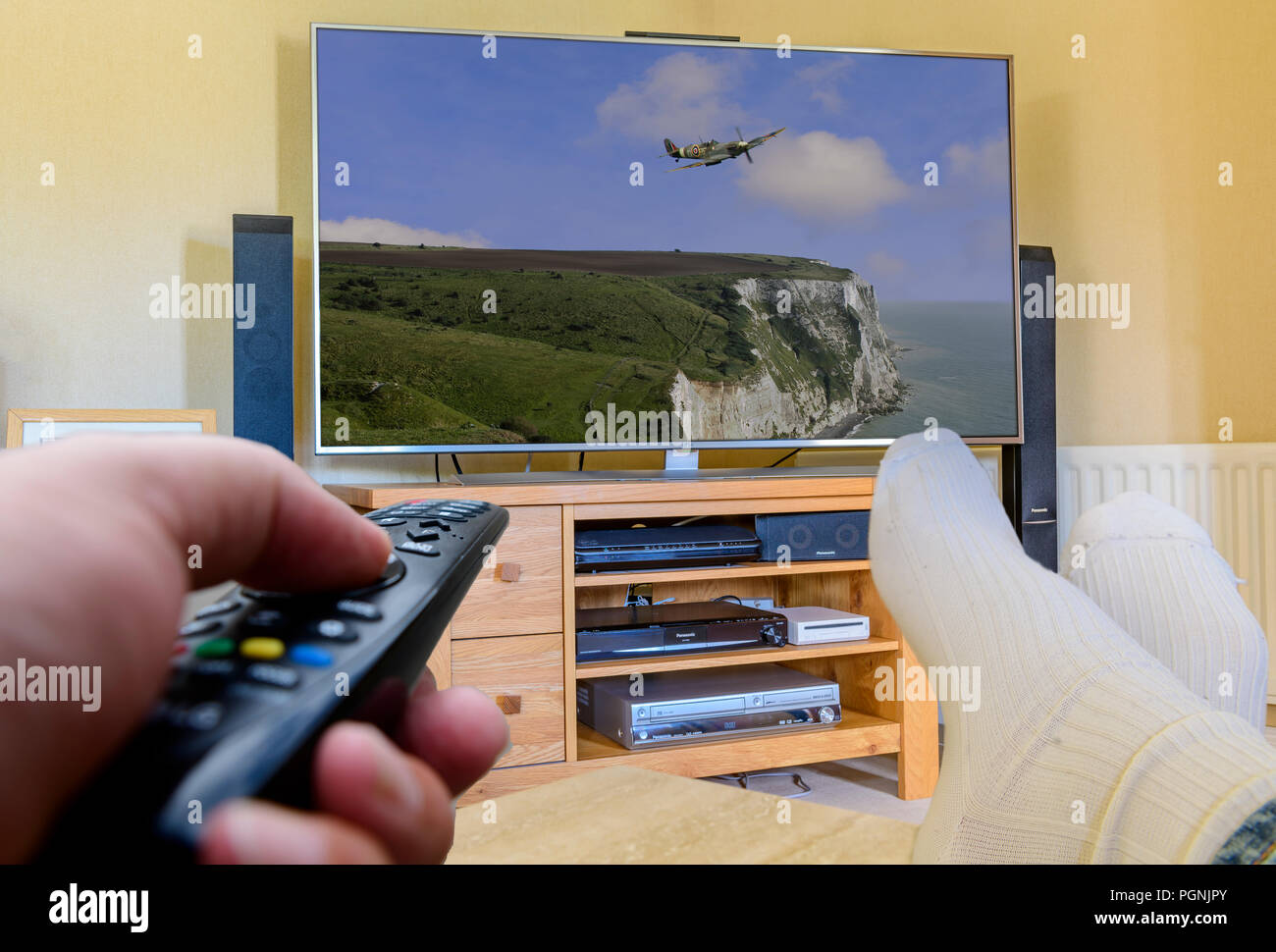 Mann mit Füßen mit Fernbedienung TV-Kanäle zu ändern. Stockfoto