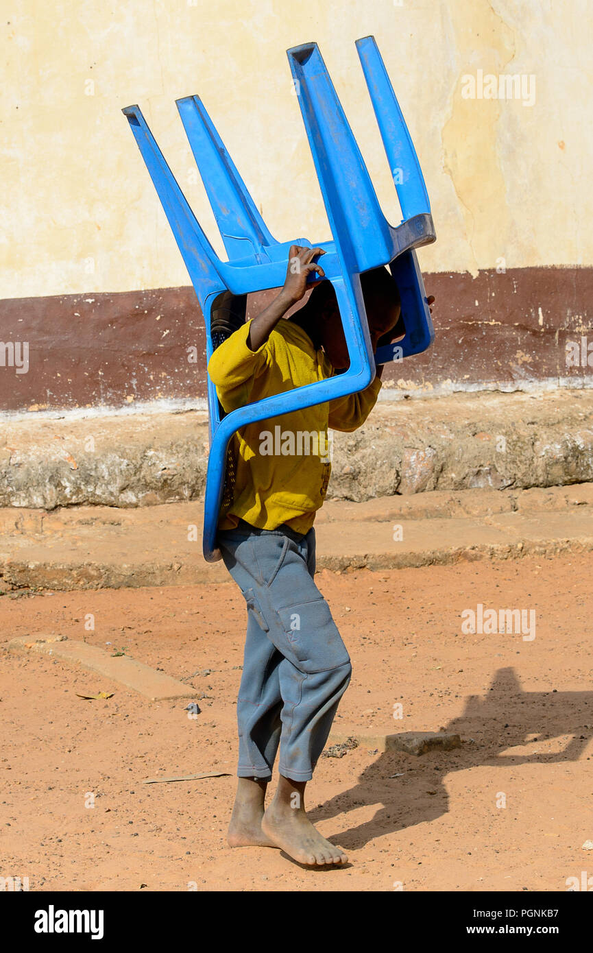 KARA REG., TOGO - Jan 14, 2017: Unbekannter Konkomba kleiner Junge trägt eine blaue Stuhl aus Kunststoff im Dorf. Konkombas sind ethnische Gruppe von Togo Stockfoto