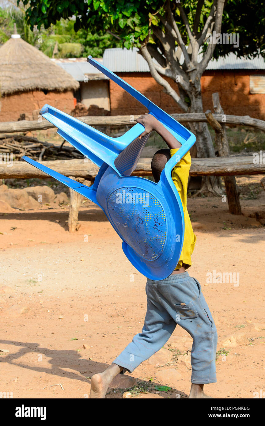 KARA REG., TOGO - Jan 14, 2017: Unbekannter Konkomba kleiner Junge trägt eine blaue Stuhl aus Kunststoff im Dorf. Konkombas sind ethnische Gruppe von Togo Stockfoto