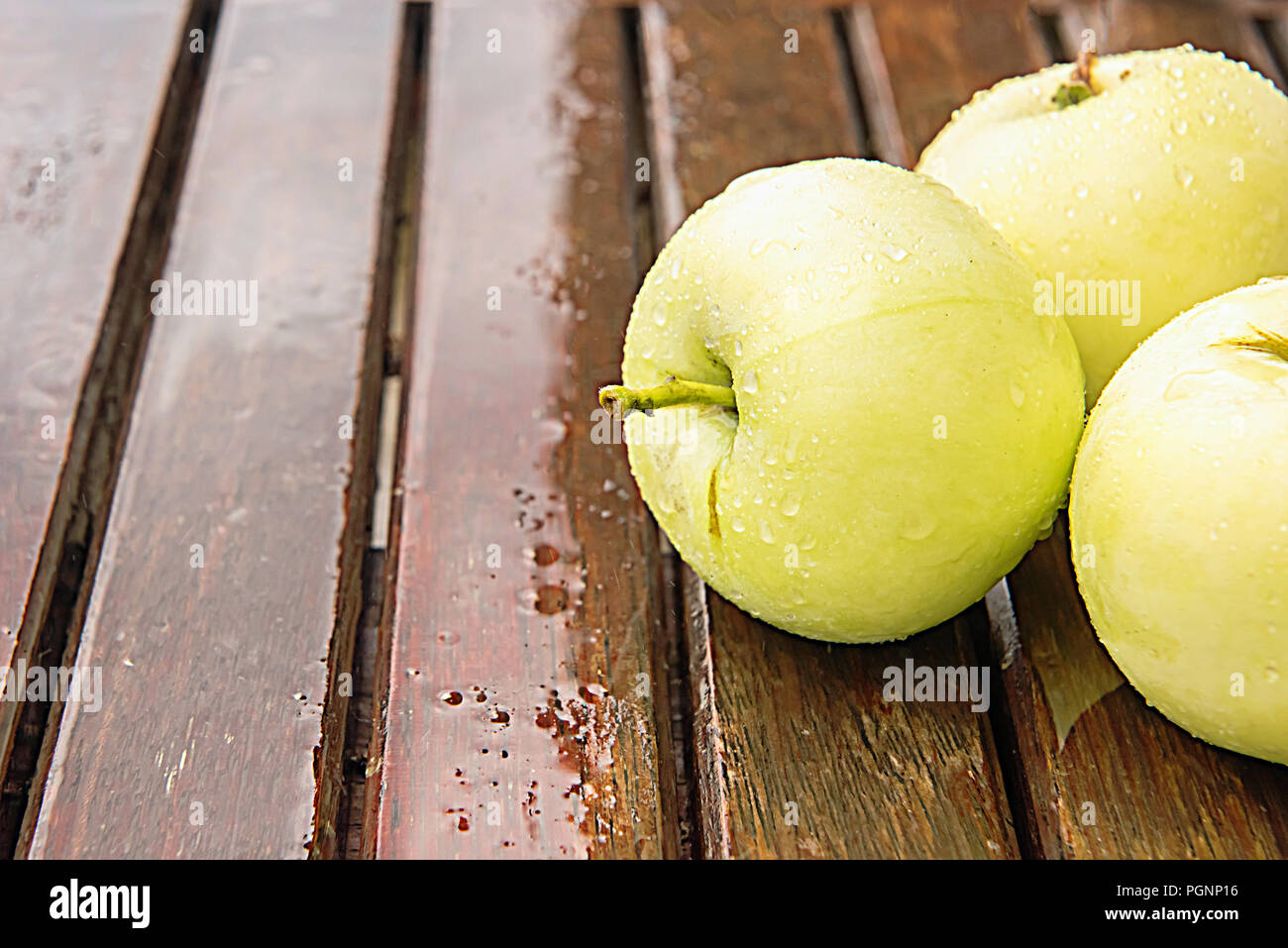 Drei nass Golden grüne Äpfel mit Wassertropfen auf braun nassen natürlichen alten Holztisch Oberfläche bedeckt. Hintergrund mit reifen Früchten und Kopieren. Stockfoto