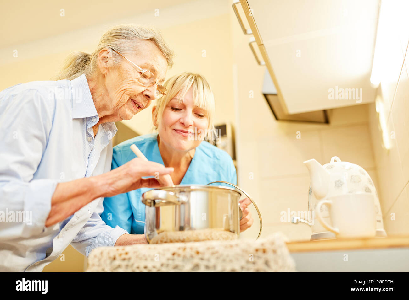Soziale Dienst Frau und älterer Bürger in der Küche der Senioren Apartment beim Kochen Stockfoto