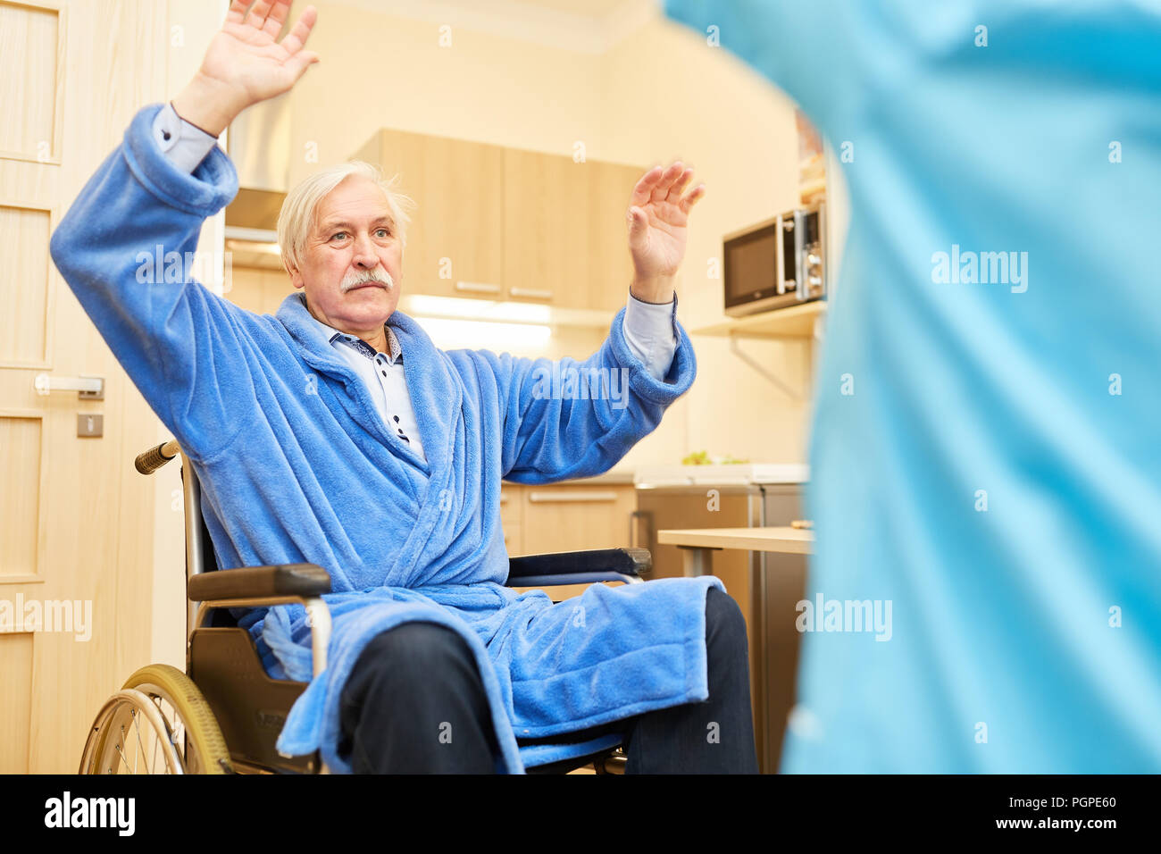 Älterer Mann im Rollstuhl wirft die Hände am rehab Übung in der Physiotherapie Stockfoto