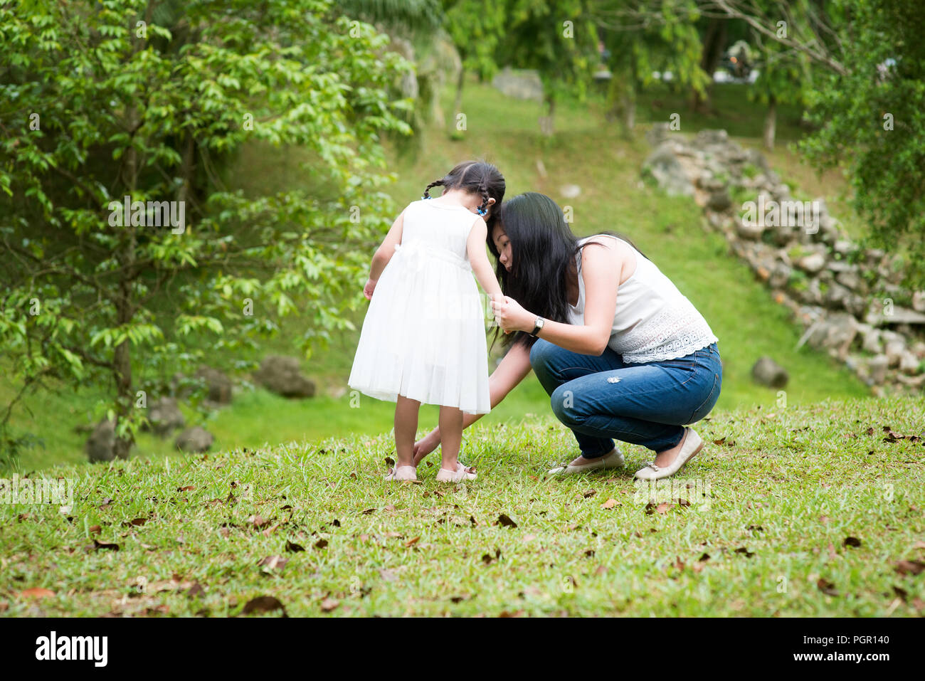 Mutter hilft, kleine Mädchen Schuh tragen im Park. Asiatische Familie im Freien portrait. Stockfoto