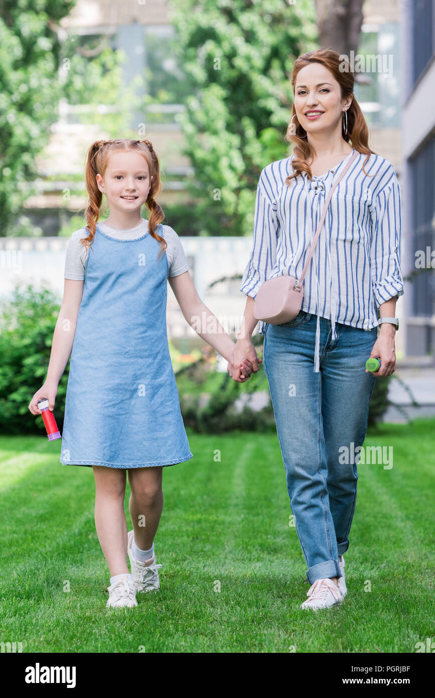 Lächelnde Mutter und Tochter mit Seifenblasen halten sich an den Händen Stockfoto