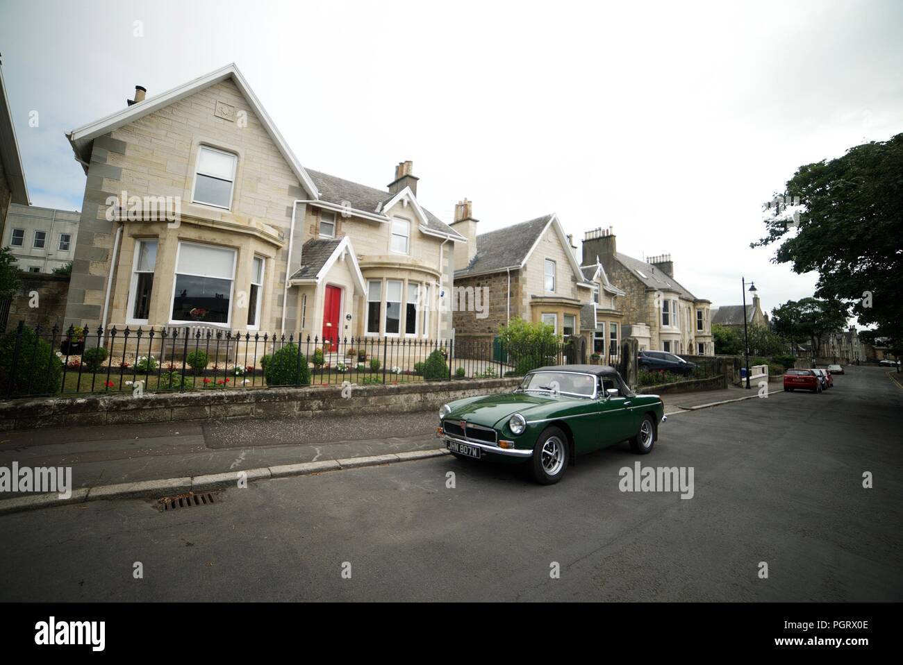 Oldtimer (dunkelgrün MG Roadster?) Auf der Straße vor einigen Häusern geparkt Stockfoto