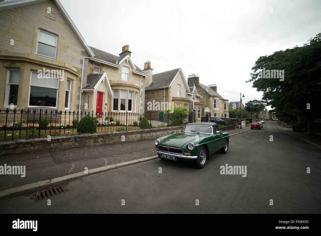 Oldtimer (dunkelgrün MG Roadster?) Auf der Straße vor einigen Häusern geparkt Stockfoto