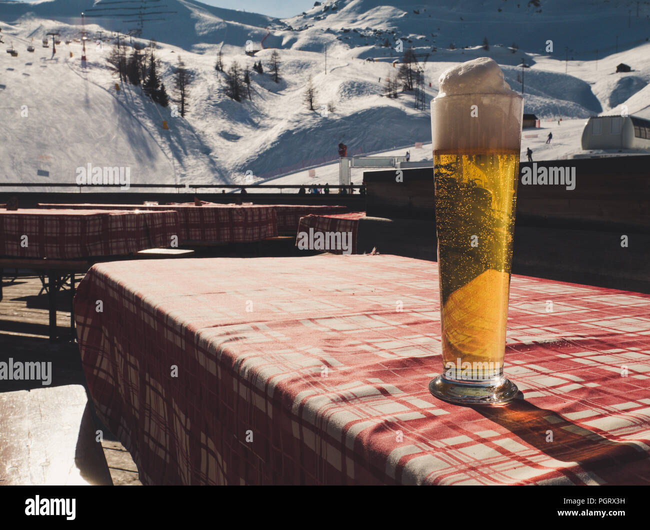 Großes Bier auf den Tisch, ein rot-weißes Karomuster Tuch. Winterlandschaft im Hintergrund mit Skipiste. Vintage Style. Stockfoto