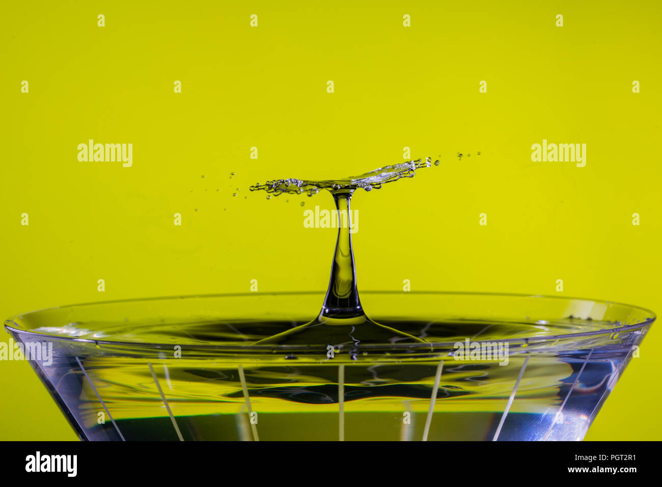 Eine fallende Tropfen kollidiert mit einem steigenden splash Spalte über ein Martini Glas, erstellen eine flache Scheibe des strahlenden Spray. Stockfoto