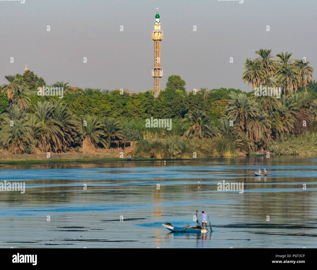 Ägyptische lokaler Mann in alten Ruderboot fischen mit Netz im frühen Sonnenlicht, mit hohen Moschee Minarett, Nil, Ägypten, Afrika Stockfoto