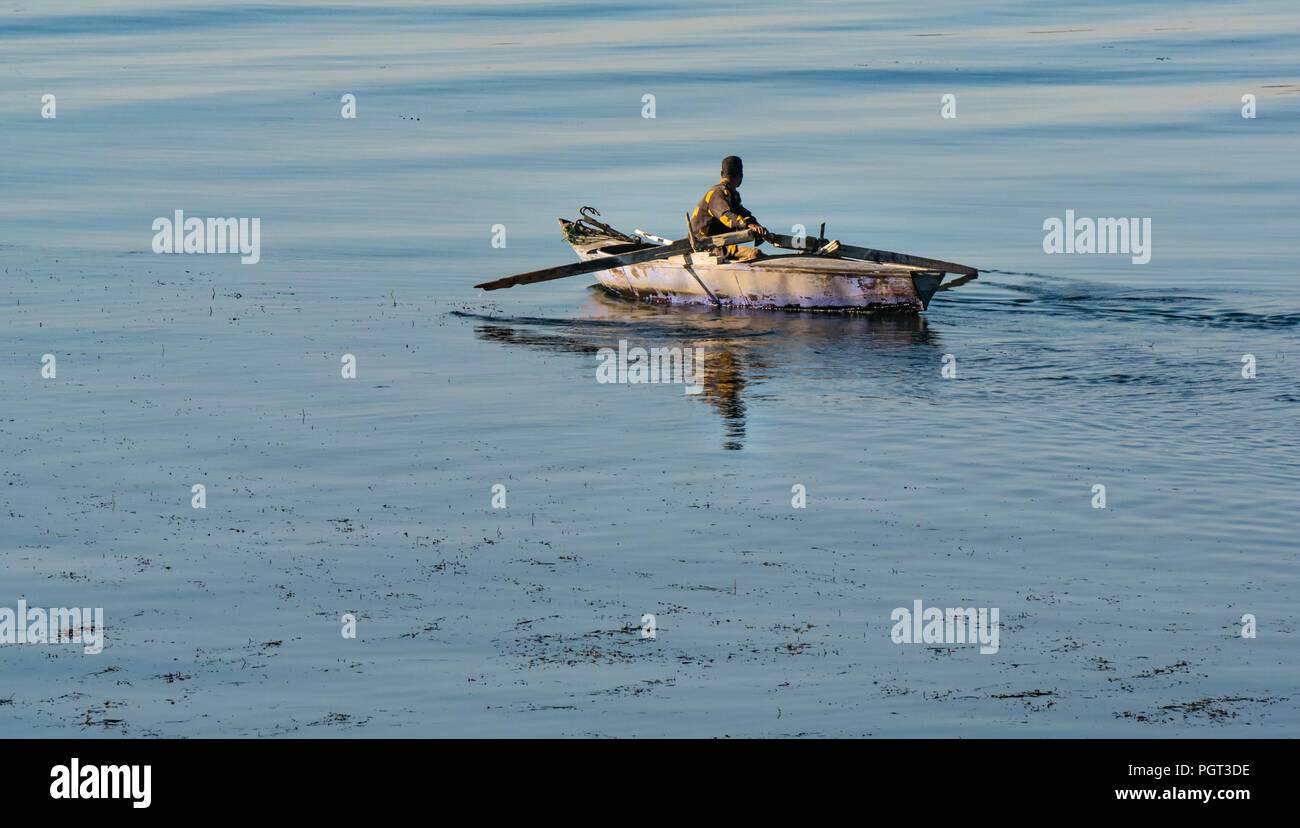 Ägyptische lokaler Mann rudern altes Boot mit Ruder in der frühen Morgensonne, mit Wasser Reflexionen, Nil, Ägypten, Afrika Stockfoto