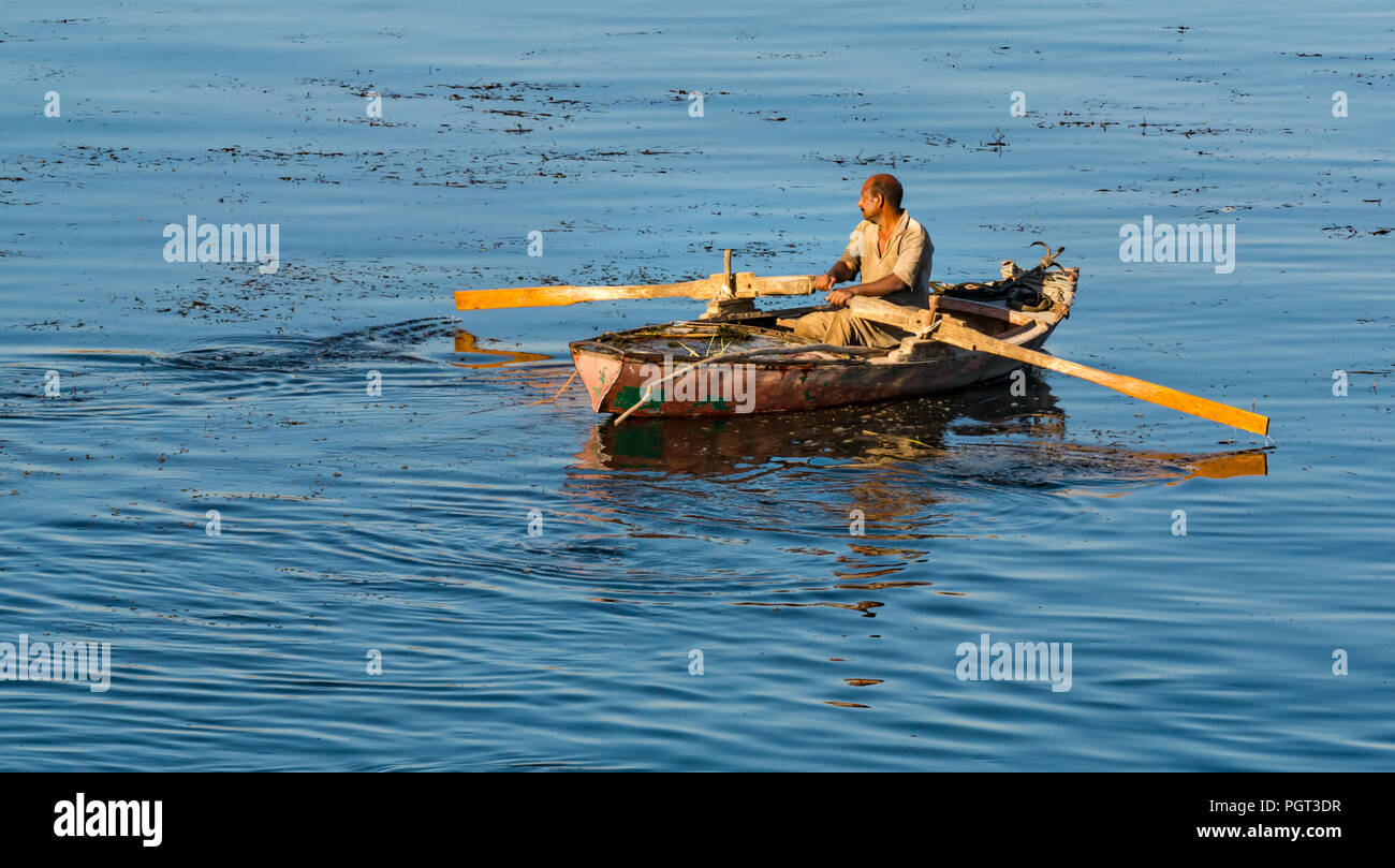 Ägyptischen Mann im Ruderboot mit Rudern am frühen Morgen Licht, am Kamera suchen, mit glatten Wasser Reflexionen, Nil, Ägypten, Afrika Stockfoto