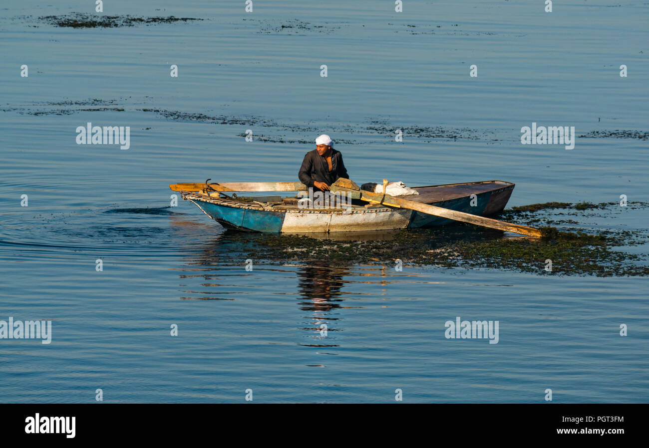 Ägyptische lokale Mann mit Turban in alten Ruderboot mit Rudern im Morgenlicht mit Wasser Reflexionen, Nil, Ägypten, Afrika Stockfoto
