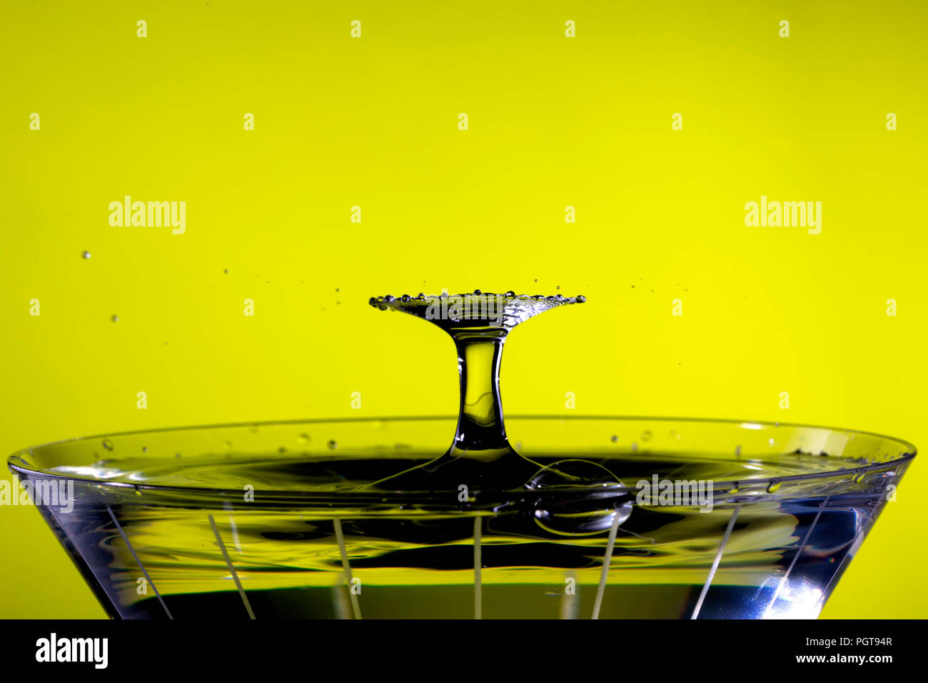 Tröpfchen kollidieren oben Martini Glas, wodurch ein radiallüfter Muster. Hintergrund ist gelb/ Stockfoto
