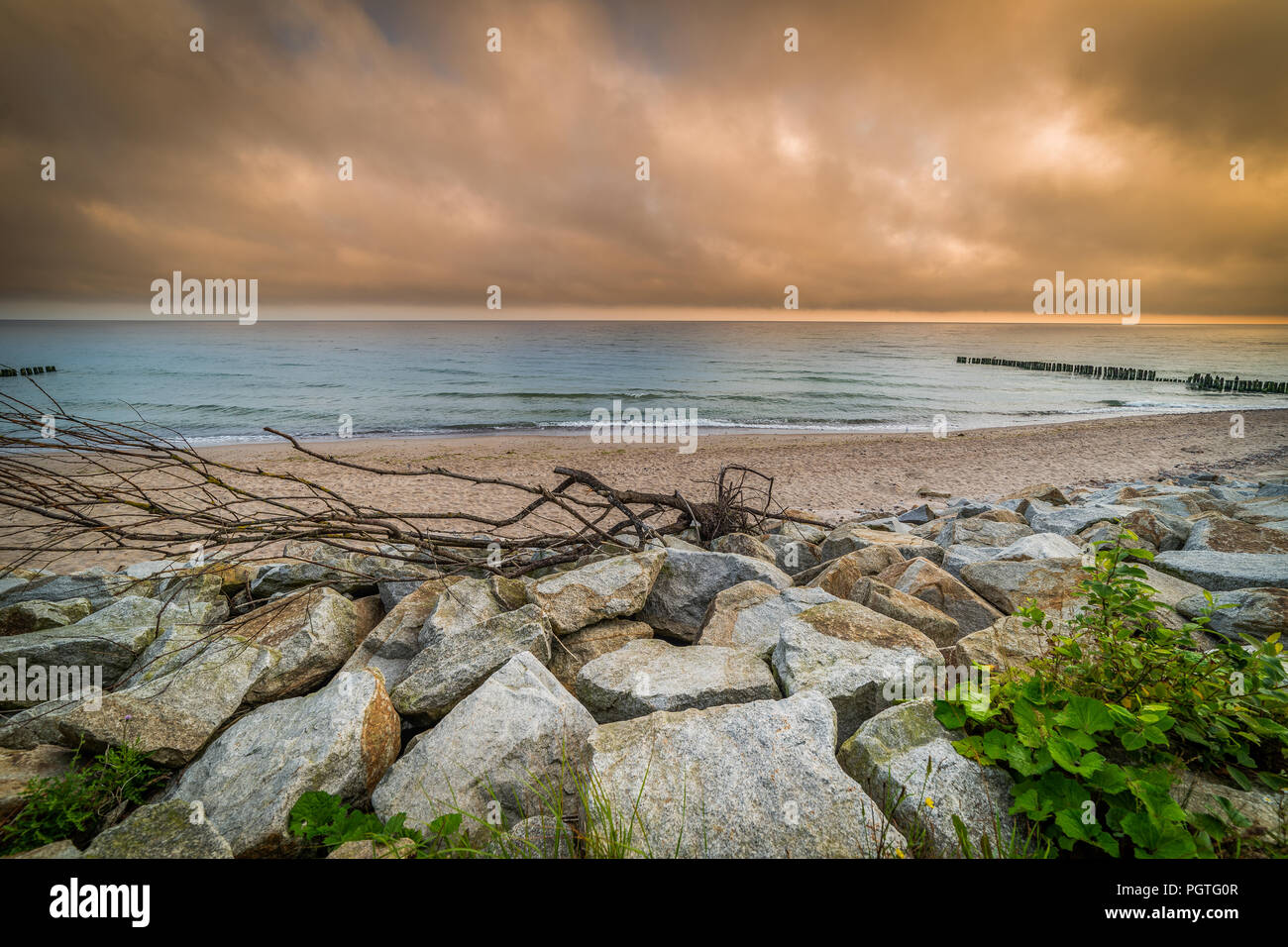 Landschaft am Meer, Holz, Steine, Sand, Wellen. orange bewölkter Himmel Stockfoto