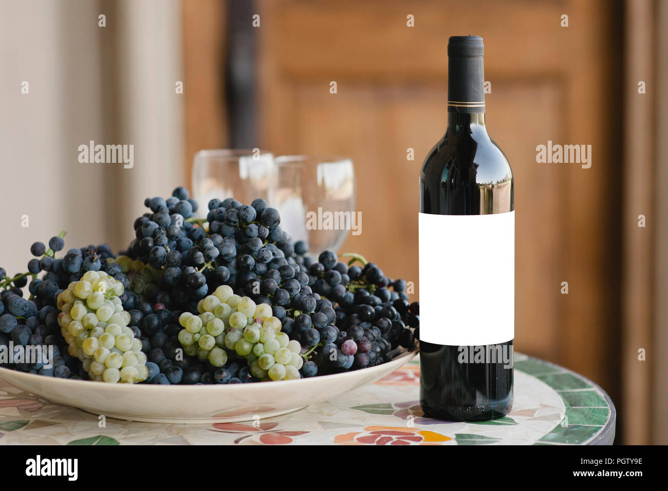Leeres Etikett auf einer roten Flasche Wein neben einer Weintraube Stockfoto
