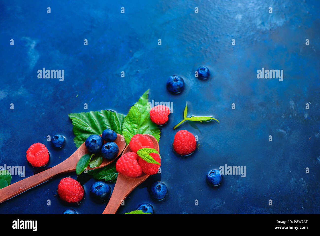 Close-up Sommer Beeren in Holz- spoonsRaspberry und blueberry Mix auf einem dunkelblauen nass Hintergrund mit kopieren. Zutaten Header Stockfoto