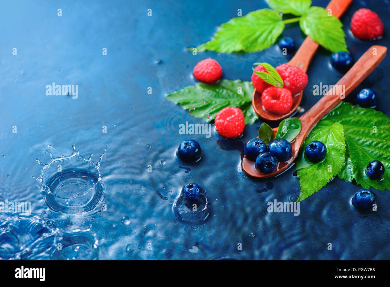 Sommer Beeren in der Kochlöffel mit Regentropfen. Himbeeren und Blaubeeren mix auf einem dunkelblauen nass Hintergrund mit kopieren. Zutaten Konzept Stockfoto