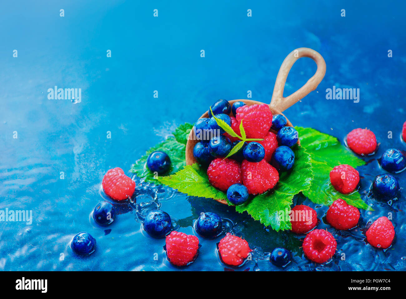 Sommer Beeren in einem runden hölzernen Löffel mit Regentropfen. Himbeeren und Blaubeeren mix auf einem dunkelblauen nass Hintergrund mit kopieren. Zutaten Konzept Stockfoto