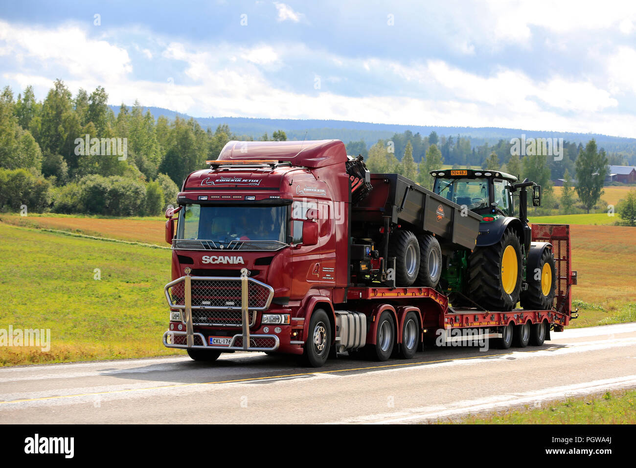 JAMSA, Finnland - 27. AUGUST 2018: Rote Scania R450 Lkw Hols landwirtschaftlichen Traktor und Anhänger entlang der Straße über die finnische Landschaft im Spätsommer Stockfoto