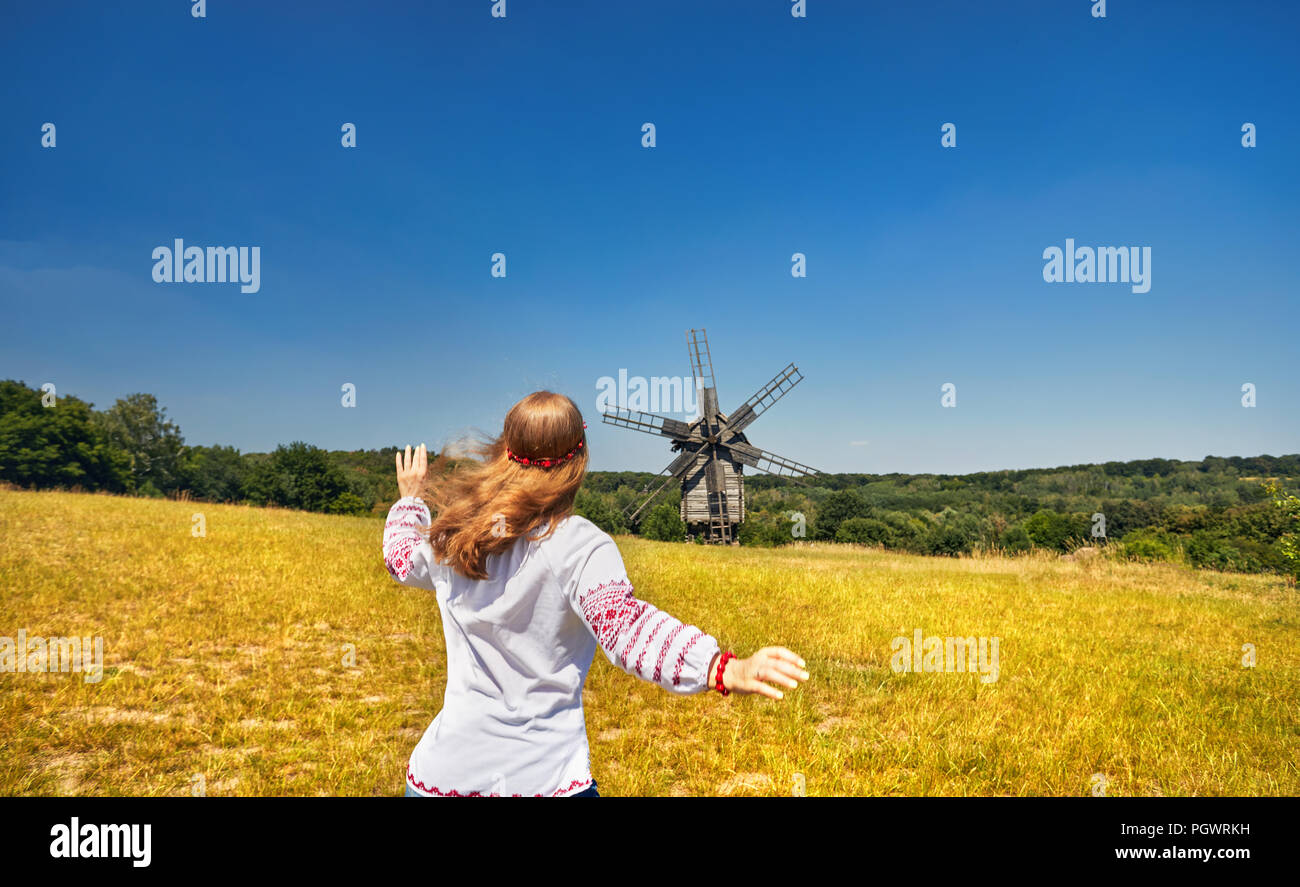 Schöne Ukrainische Mädchen zu laufen, um hölzerne Windmühle in weißen ethnischen Shirt auf nationaler Architektur Museum in Pirogowo. Kiew, Ukraine Stockfoto